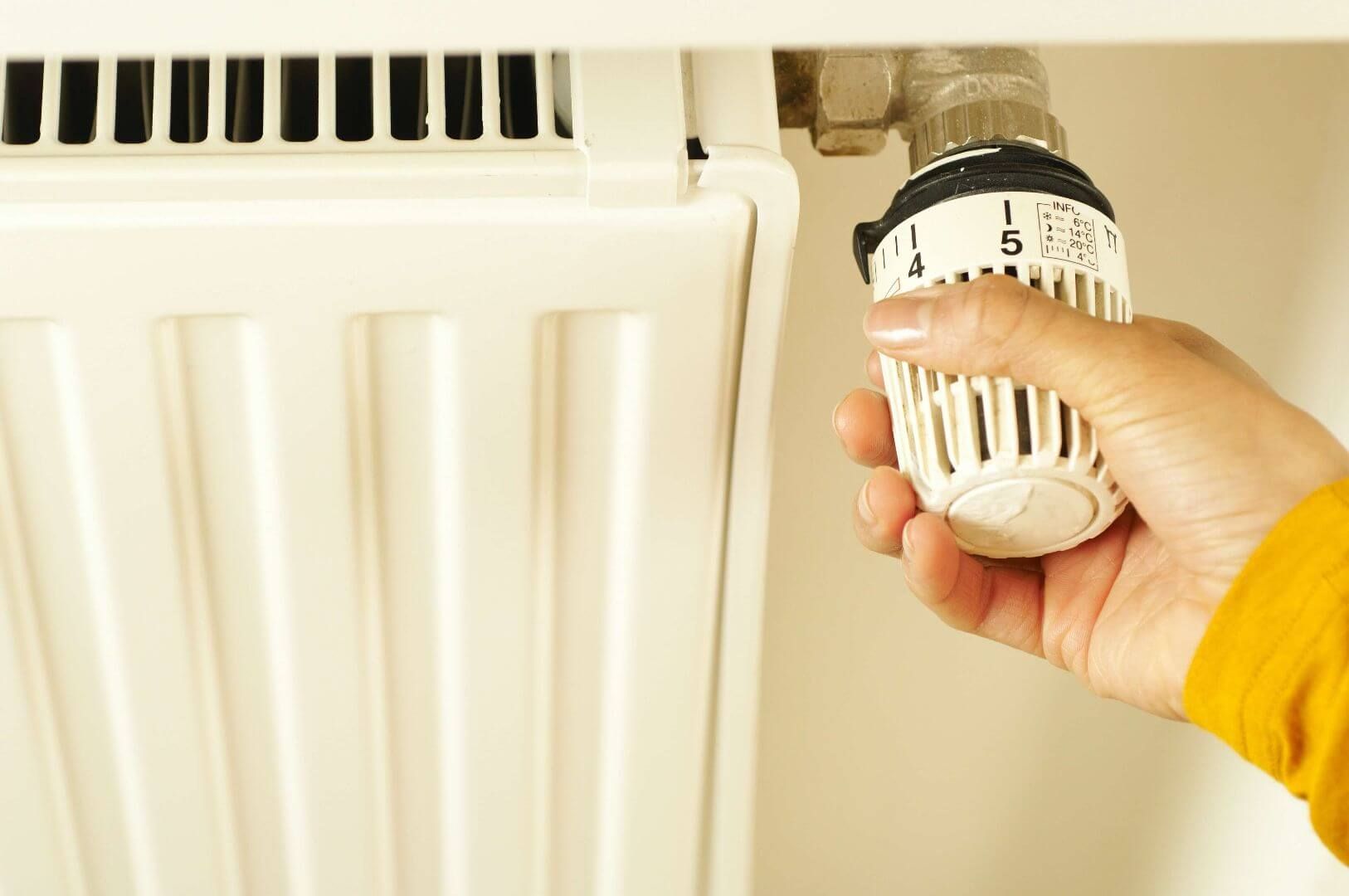 Ręka przekręcająca głowicę termostatyczną na grzejniku.
