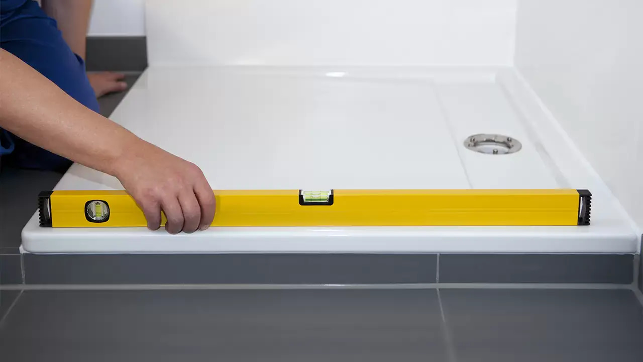 Instalator sprawdza poziom montowanego brodzika przy pomocy ż&oacute;łtej poziomicy.