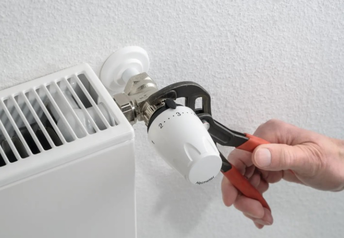 Dłoń dokręcająca głowicę termostatyczną za pomocą klucza